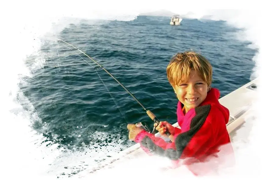 A young boy is holding onto a rope while riding on the water.